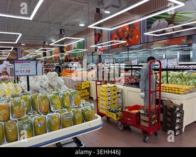 Ouvrier organisant des fruits dans un supermarché asiatique, entouré de divers fruits et légumes exposés. Banque D'Images