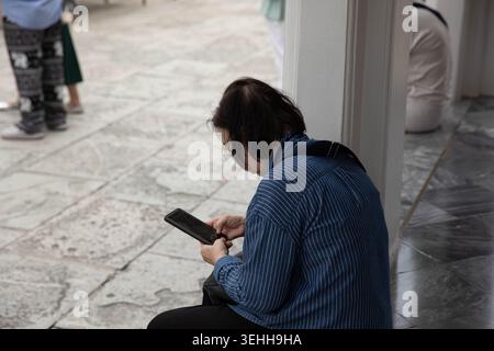 Femme âgée se reposant et utilisant un smartphone, absorbé dans l'écran mobile, utilisateur de smartphone concentré, profil latéral. Banque D'Images
