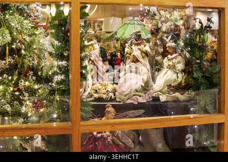 Regardez à travers un cadre de fenêtre en bois une exposition de scènes de la crèche de Noël avec les figurines de trois hommes sages et des pins illuminés. Banque D'Images
