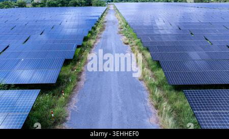 Des rangées de panneaux solaires utilitaires flanquent une route de service rurale qui démontre l'infrastructure durable des énergies renouvelables à Khon kaen thaïlande. Banque D'Images