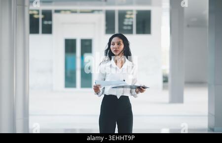 Portrait pleine longueur d'une femme d'affaires confiante tenant des documents et une planche à pince dans un immeuble de bureaux lumineux, idéal pour la direction, plann d'entreprise Banque D'Images