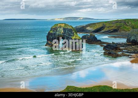 Vue côtière panoramique de l'arc en pierre naturelle de la pile de mer Virgin Rock à Nuns Beach avec des reflets de nuages sur le sable et l'eau turquoise, Kerry Irlande. Banque D'Images