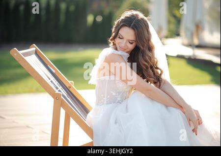 Mariée en robe blanche se relaxant sur une chaise longue à l'extérieur sur une journée ensoleillée Banque D'Images