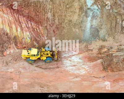 Vue aérienne d'une chargeuse sur pneus jaune travaillant dans une carrière avec de la terre rougeâtre et des parois rocheuses abruptes Coimbra, district de Coimbra, Portugal. Banque D'Images