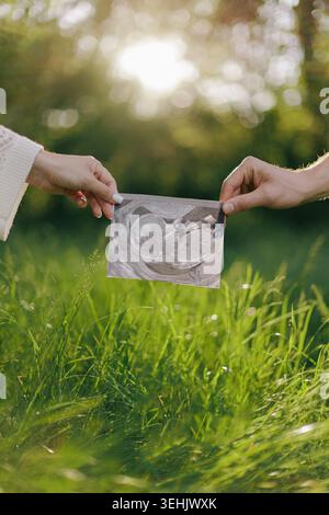 Homme et femme tenant l'image de sonogramme ensemble au-dessus de l'herbe verte. Gros plan de futurs parents montrant une échographie dans un parc d'été sous un soleil éclatant Banque D'Images