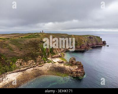 Un panorama suggestif de la côte bretonne au Cap Fréhel, avec le phare à l’horizon et une baie sauvage au premier plan. Falaises de grès rose pl Banque D'Images