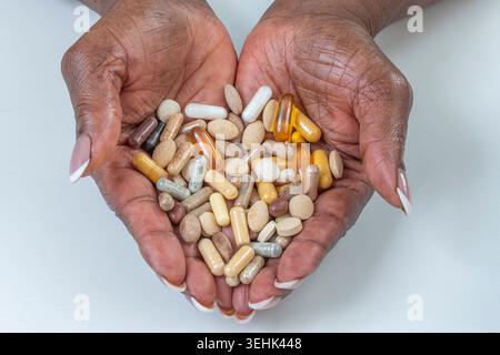 Deux mains humaines tiennent une variété de capsules pharmaceutiques et de comprimés de différentes couleurs, formes et tailles. Banque D'Images