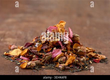 Un tas de pétales et de bourgeons de rose séchés (Rosa) est mélangé avec des feuilles de thé séchées sur une surface en bois. Banque D'Images