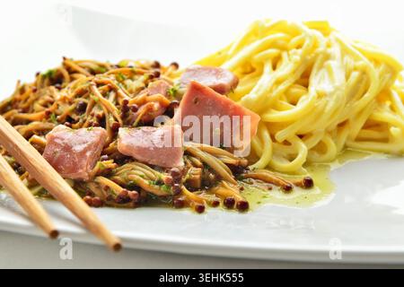 Jambon avec champignons enoki dorés et pâtes avec baguettes sur table blanche. Plat simple très juteux de la cuisine asiatique Banque D'Images