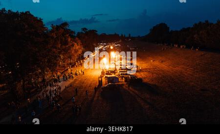 Vue aérienne des brûleurs de montgolfières éclairant un festival nocturne avec des foules de gens et des véhicules garés à Senta, Voïvodine, Serbie. Banque D'Images