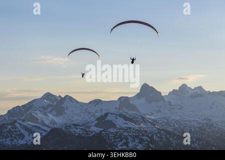 Vue aérienne de deux parapentes survolant les sommets enneigés de Hoher Dachstein sous un ciel bleu clair Liezen District, Styrie, Autriche. Banque D'Images