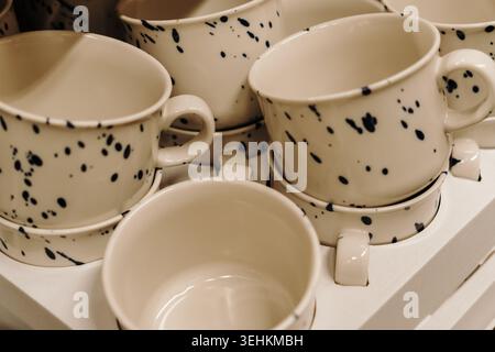 Tasses en céramique décoratives avec motif à pois noirs exposées dans un magasin d'articles ménagers. Concept d'ustensiles de cuisine élégants pour café et branding d'intérieur. Banque D'Images