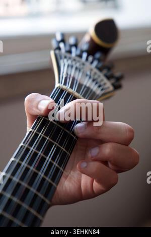 Gros plan d'une main tenant le cou d'une guitare portugaise traditionnelle, affichant des doigts appuyant sur les cordes tout en jouant de la musique Fado Banque D'Images
