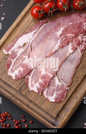 Nourriture, tranches de délicieux jamon fumé ou prosciutto avec du sel, des épices et des herbes sur un fond de béton foncé Banque D'Images