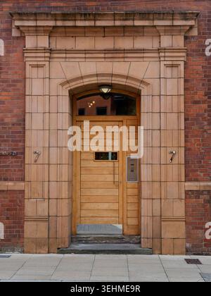 Une porte victorienne voûtée en grès avec une porte contemporaine en bois et un panneau d'interphone, 7 Hulme Street, Oxford Road corridor, Manchester. Banque D'Images