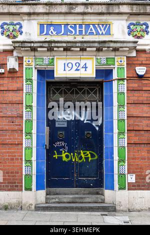 Porte carrelée Art Nouveau de J&J Shaw, datée de 1924, avec graffiti sur la porte bleue, New Wakefield Street, Manchester. Banque D'Images