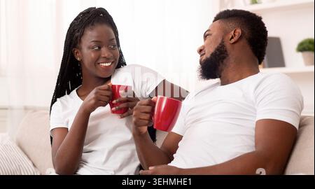 Jeune couple afro-américain se relaxant à la maison, buvant du café et discutant Banque D'Images
