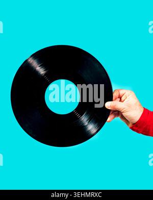 Gros plan d'une main tenant un disque vinyle noir sur fond turquoise lumineux, style pop art minimal avec espace de copie, évoquant la musique rétro Banque D'Images