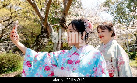 La femme chinoise et sa mère portent un kimono coloré dans le parc de Maruyama, au Japon, prenant un selfie sous les fleurs de cerisier un jour de printemps ensoleillé, célébrant Banque D'Images