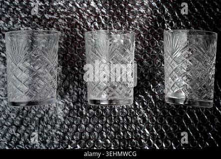 Trois gobelets en verre coupé disposés sur un emballage à bulles foncées, montrant la texture plastique protectrice, le concept d'emballage, la sécurité d'expédition et le gla fragile Banque D'Images