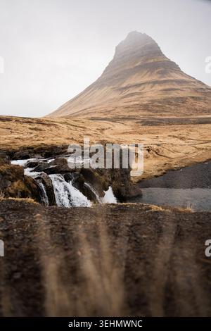 Vue atmosphérique de la montagne Kirkjufell s'élevant au-dessus d'une petite cascade et paysage de lave accidenté sur la péninsule de Snaefellness, Islande, sous mi doux Banque D'Images