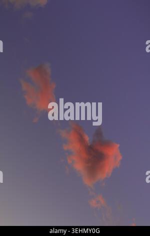 Un magnifique ciel nocturne présente des nuages doux et vibrants dispersés sur une toile de fond dégradée passant du bleu aux subtiles teintes lavande comme la lumière du soleil Banque D'Images