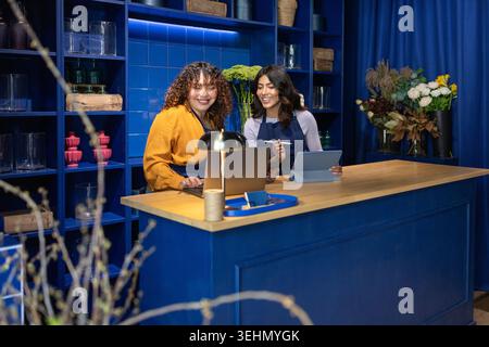 Deux fleuristes joyeux collaborent à un comptoir en bois dans un magasin de fleurs moderne aux murs bleus. Ils sont plongés dans leur travail, entourés d'un asso Banque D'Images