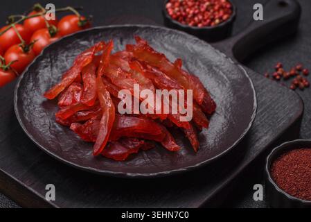 Nourriture, tranches de poulet séchées, saccadé, avec saveur de cerise ou de prune, sel et épices sur un fond de béton foncé Banque D'Images