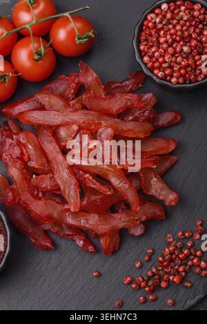 Nourriture, tranches de poulet séchées, saccadé, avec saveur de cerise ou de prune, sel et épices sur un fond de béton foncé Banque D'Images