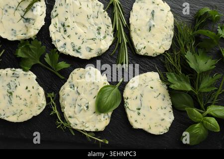 Beurre aux herbes sur la table noire, pose à plat Banque D'Images