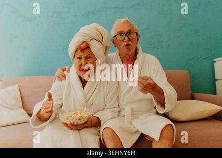 Heureux couple senior regardant la télé et mangeant du pop-corn. Banque D'Images