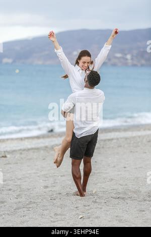 Un couple heureux apprécie leur temps ensemble à Playa del Zapillo à Almeria, en Espagne. L'homme soulève la femme joyeusement alors qu'ils célèbrent leur amour. Le t Banque D'Images