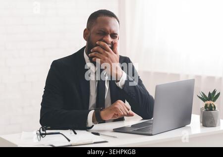 Homme d'affaires ennuyé assis dans son bureau et bâillant Banque D'Images