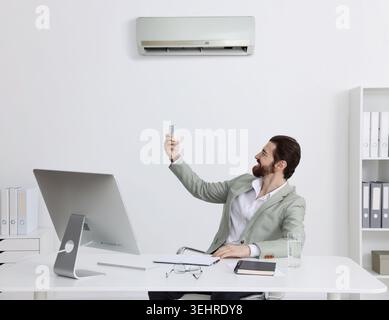Homme allumant le climatiseur dans le bureau. Environnement de travail confortable Banque D'Images
