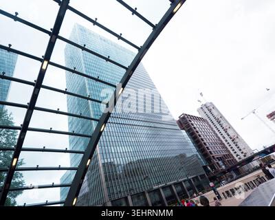 Une vue spectaculaire en bas angle des gratte-ciels de verre étincelants à Canary Wharf, Londres, encadrés par un toit en verre incurvé au premier plan. Banque D'Images
