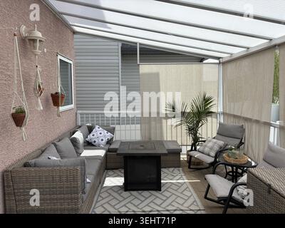 Patio couvert moderne, espace de vie extérieur confortable avec des plantes suspendues et des décorations en macramé contre un mur en stuc. Banque D'Images