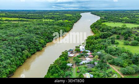 Une perspective aérienne capture la rivière sinueuse Guayabero, flanquée d'une végétation dense et d'un groupe de maisons à Guaviare, en Colombie. Banque D'Images