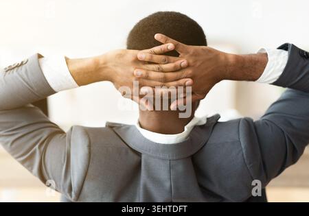 Employé africain croisant les mains derrière la tête, ayant le repos au bureau Banque D'Images