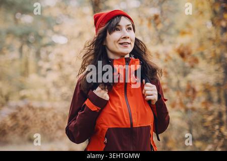 Femme souriante marche à travers la forêt d'automne avec pile de bûches de bois en arrière-plan. tourisme de nature responsable, loisirs à faible impact, écologique Banque D'Images