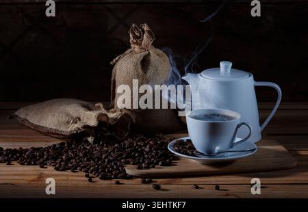 Moody Still Life de café chaud fraîchement préparé servi dans une tasse en céramique blanche et une théière avec vapeur visible. Banque D'Images