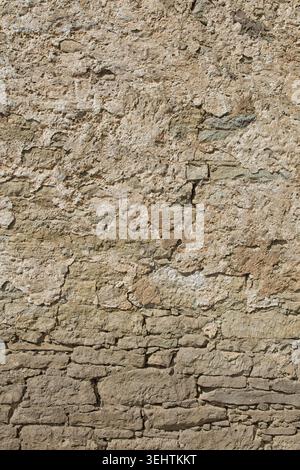 Gros plan de la texture d'un vieux mur de pierre altérée, il présente une surface fortement altérée avec un mélange de pierres apparentes. Banque D'Images