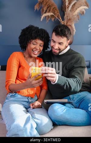 Portrait vertical couple heureux assis sur le canapé et à l'aide d'un smartphone ensemble à la maison Banque D'Images