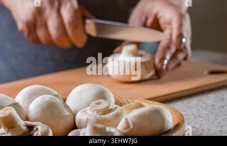 Champignons sur table en bois. Chef coupant, tranchant des champignons champignon en gros plan. Mains cuisinant des légumes sains Banque D'Images