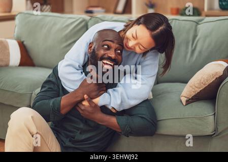Un joyeux couple interracial partage un joyeux moment de rire tout en se relaxant à la maison. Banque D'Images