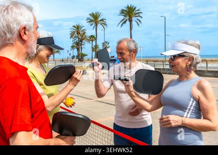 Amis seniors appréciant le pickleball sur le terrain de plage Banque D'Images
