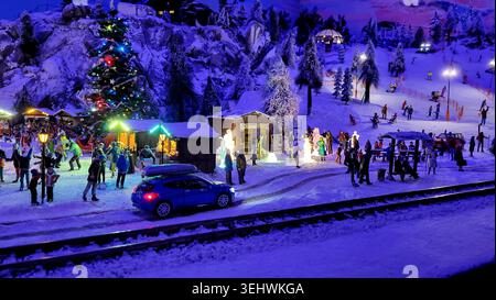 Scène de village d'hiver miniature avec voiture bleue, arbre de Noël et montagnes enneigées la nuit Banque D'Images