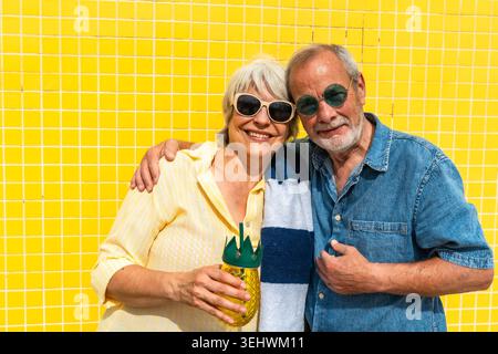 Couple senior profitant des vacances d'été contre le mur jaune Banque D'Images