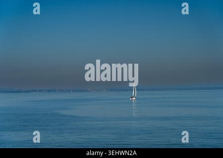 Une scène tranquille sur le lac de Constance (Bodensee) en Suisse, avec un voilier glissant doucement sur l'eau bleue calme sous un ciel vaste et clair. Banque D'Images