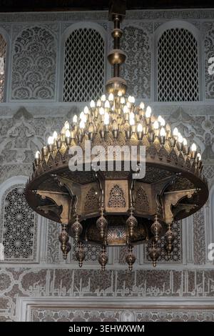 Lustre marocain orné en laiton illuminé sur un fond de sculptures complexes en stuc islamique et de calligraphie arabe dans un palais historique. Banque D'Images