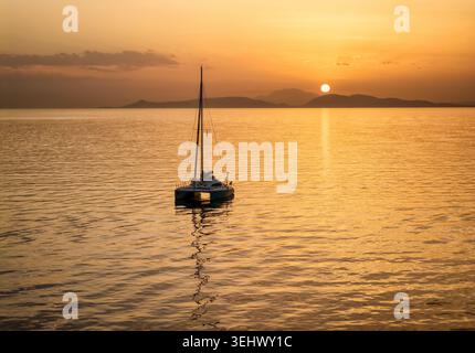 Une silhouette d'un voilier catamaran sur l'océan calme lors d'un coucher de soleil doré dans la mer méditerranée, en Grèce, en arrière-plan Banque D'Images